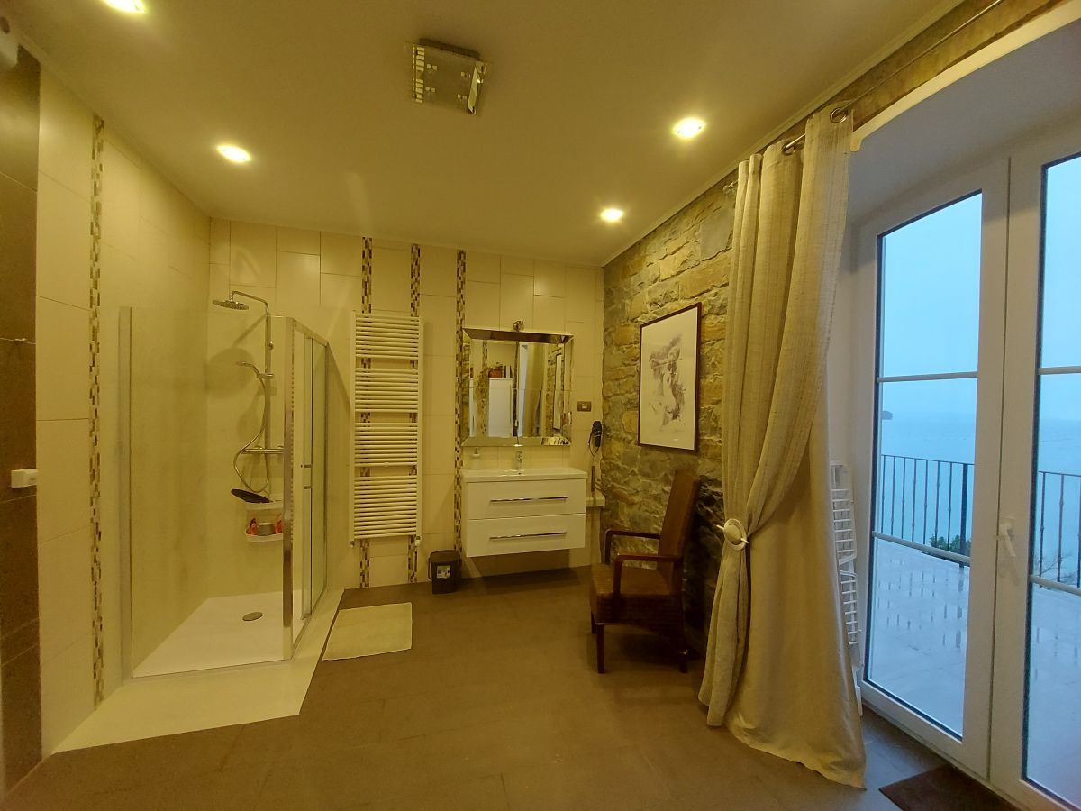 Badezimmer mit Dusche, Waschbecken mit Spiegel, Stuhl, Bild an der Wand und einer Glastür zum Balkon