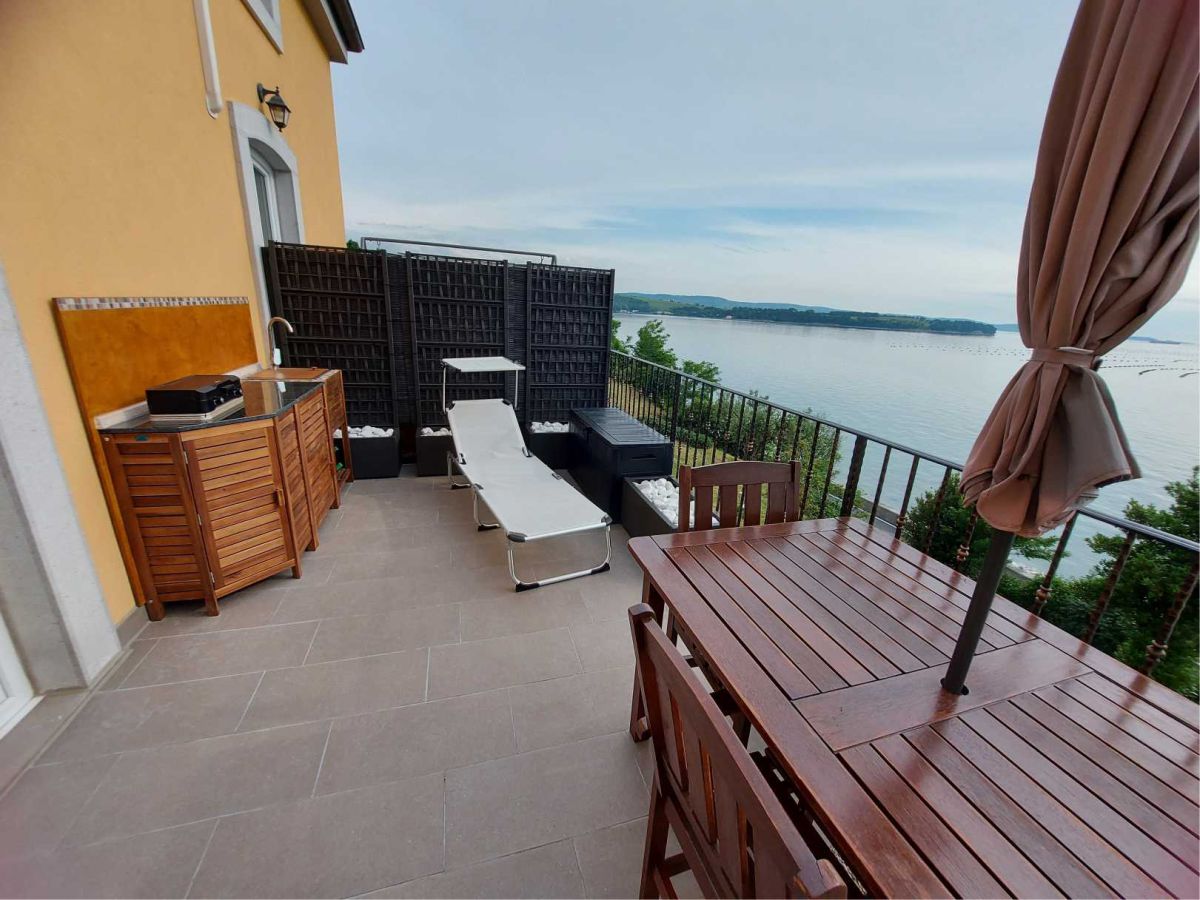 Terrasse mit Kochnische, Liege, Sonnenschirm, Tisch mit Stühlen, im Hintergrund das Meer