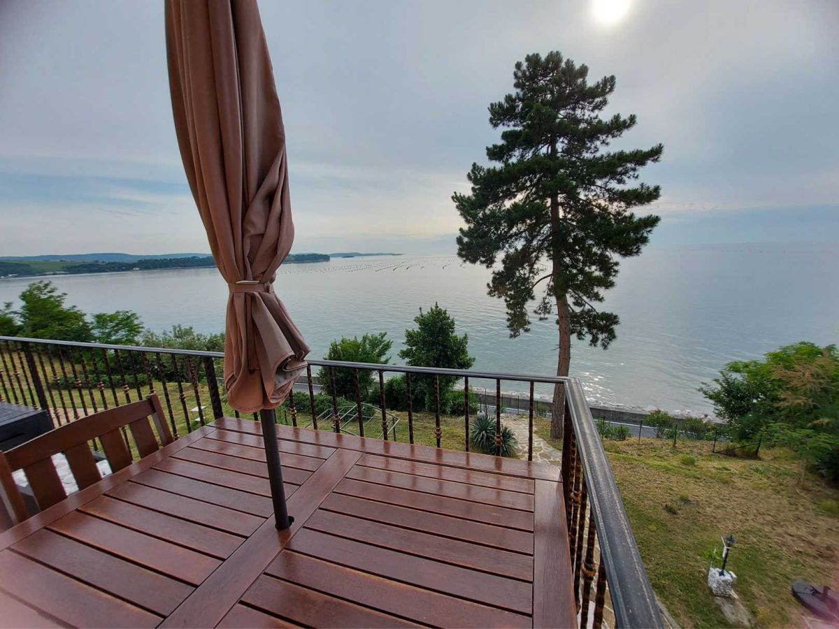 A parasol, a table with a chair, a tree with bushes, and the sea in the background