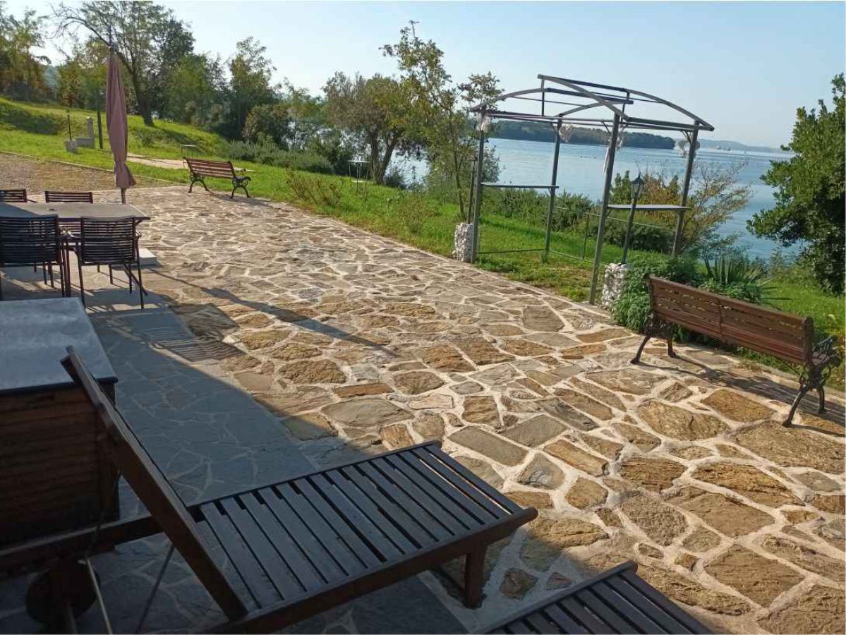 pavimento in pietra, sedie e sdraio, prato con alberi e mare sullo sfondo